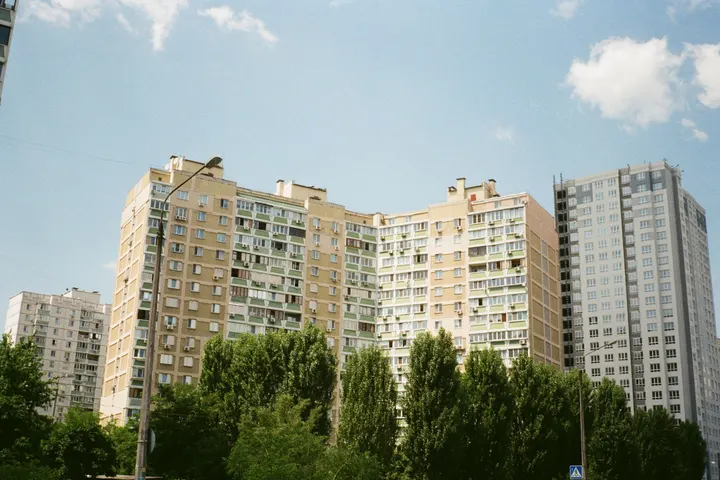 Багатоповерхівки за деревами під блакитним небом