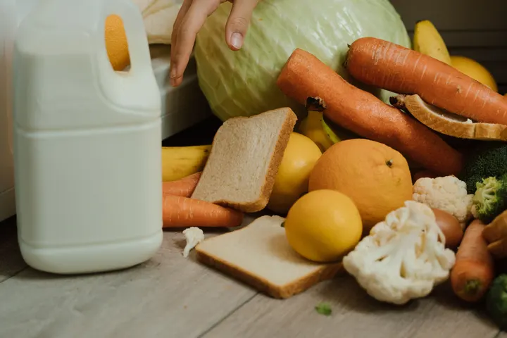 Людина збирає продукти, що випали з відкритого холодильника, з підлоги кухні